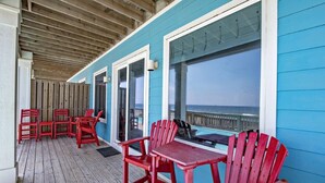 A covered outdoor area with a wooden deck, red Adirondack chairs, and a view of the ocean. - BeachFront 9Bed EasyBreezy East (Gulf Shores)