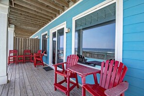 A covered outdoor area with a wooden deck, red Adirondack chairs, and a view of the ocean. - BeachFront 9Bed EasyBreezy East (Gulf Shores)