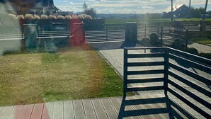 A wooden deck with a metal railing, a grassy area, and a building in the background.