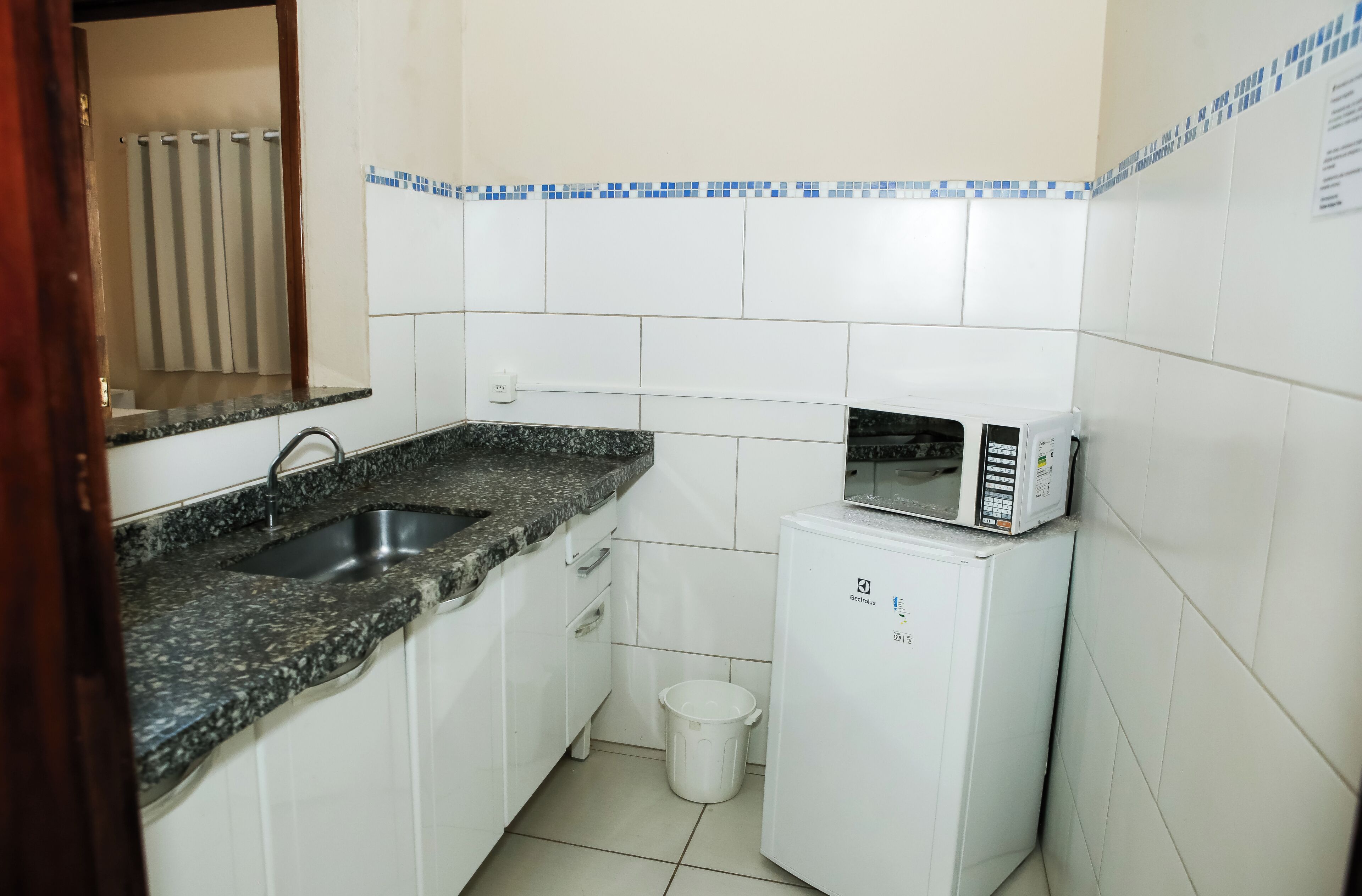 Uma cozinha compacta com bancada de granito, pia, micro-ondas e lixeira.