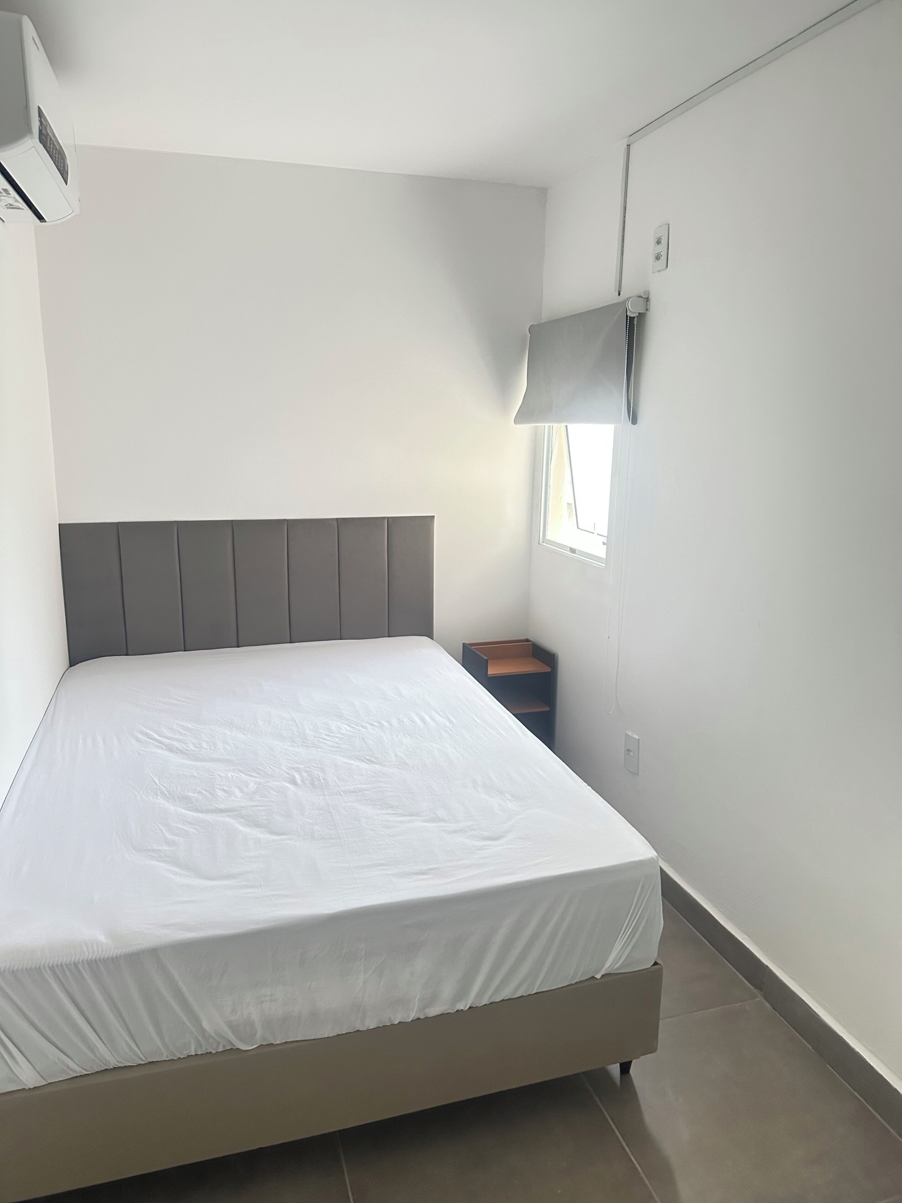 A bedroom with a bed, a nightstand, a lamp, and a window.