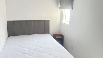 A bedroom with a bed, a nightstand, a lamp, and a window.