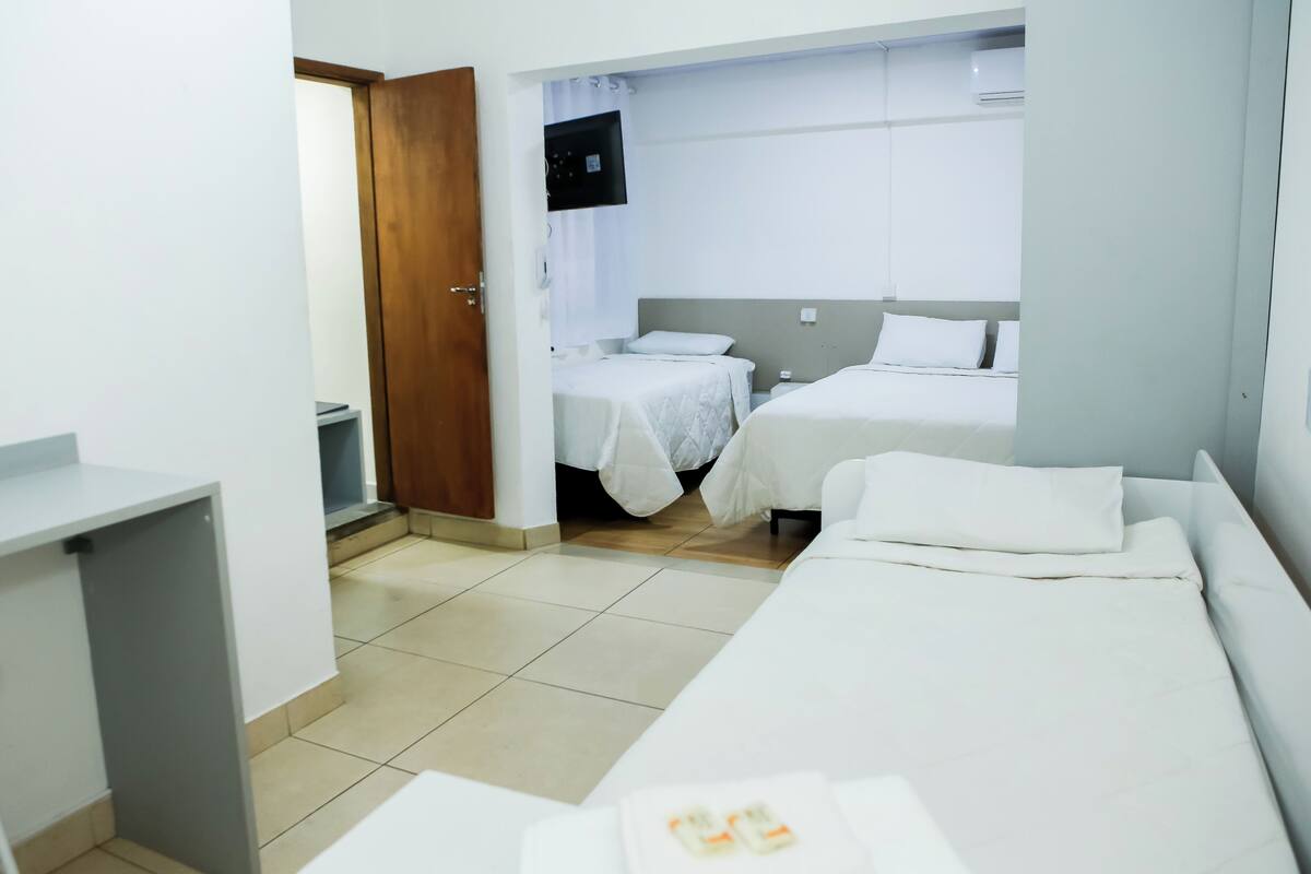 Quarto de hotel com cama, escrivaninha, cadeira e televisão fixada na parede.