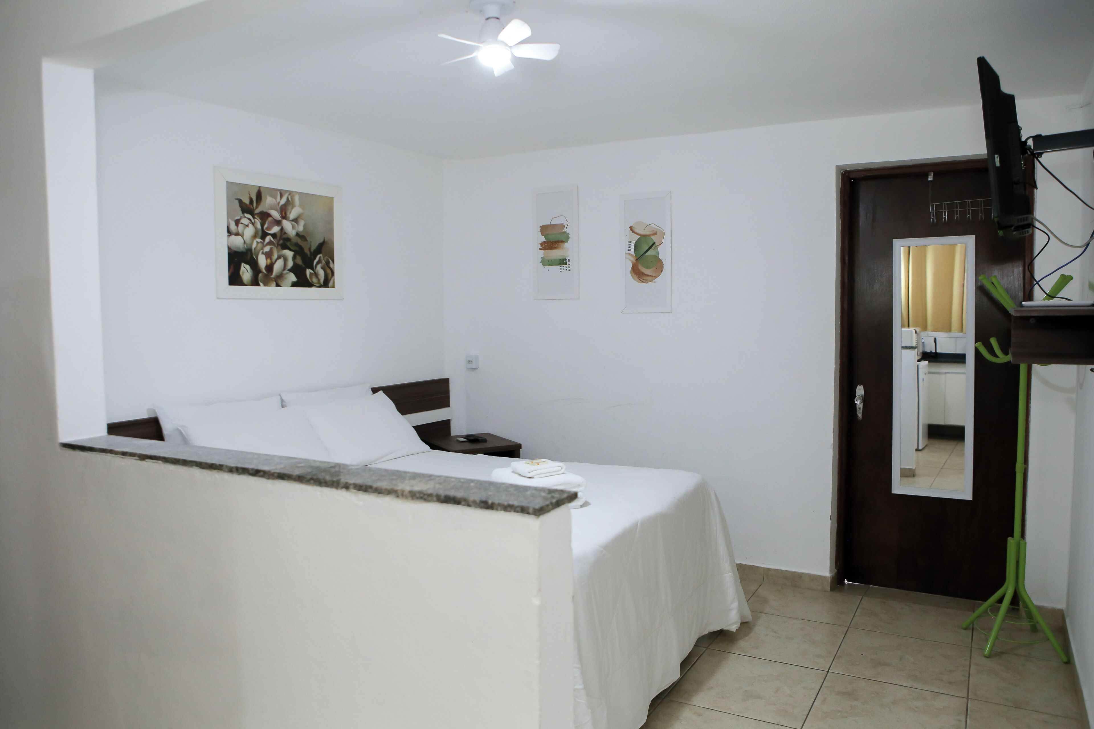 A hotel room with a bed, a nightstand, a ceiling fan, and a door with a mirror.