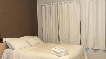 A hotel room with a bed, white curtains, a wall-mounted air conditioner, and a tiled floor.