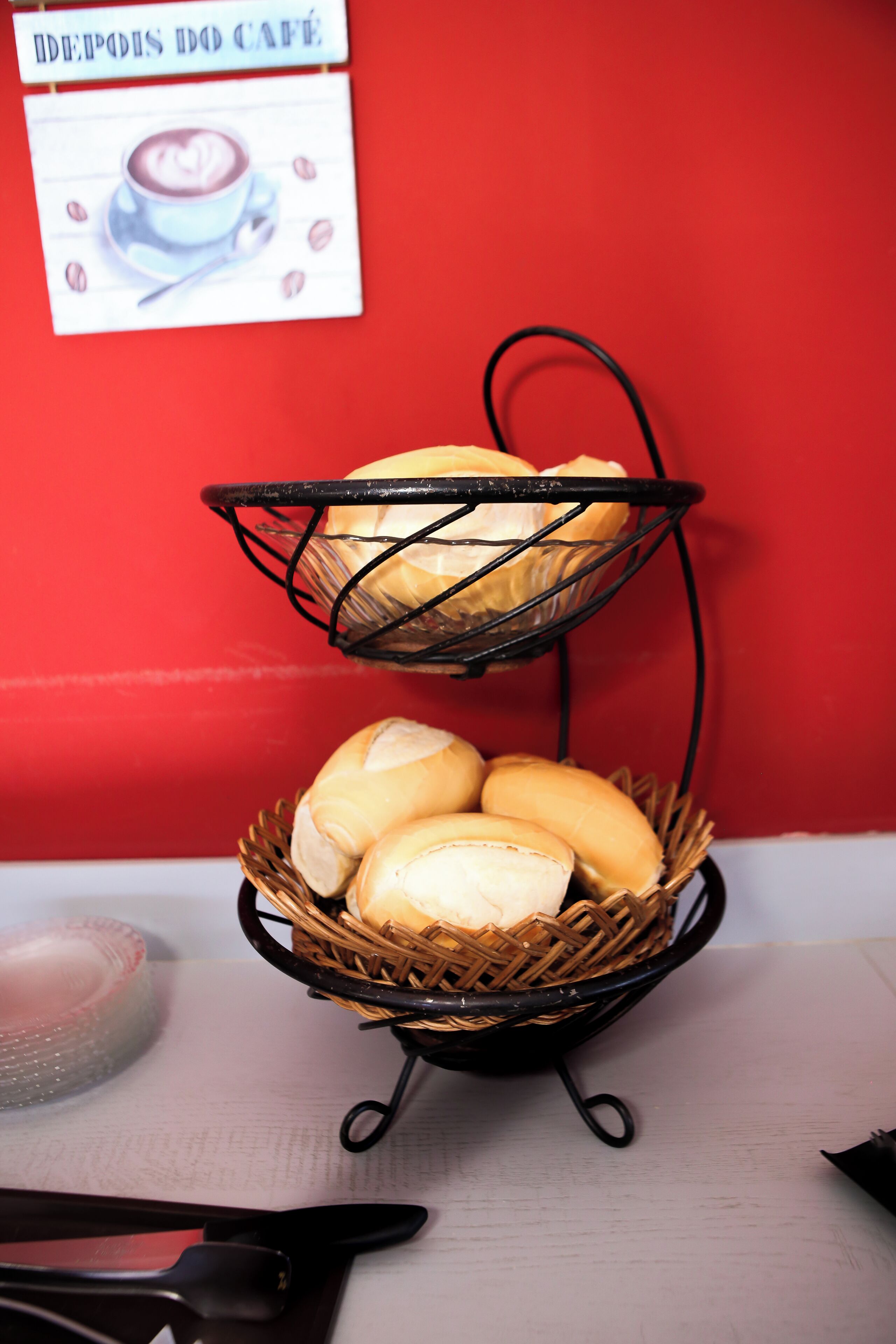 A wicker basket with bread on a table against a red wall.