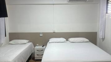 Quarto com duas camas de solteiro, mesa de cabeceira com abajur, ar condicionado fixado na parede e janela com persianas.
