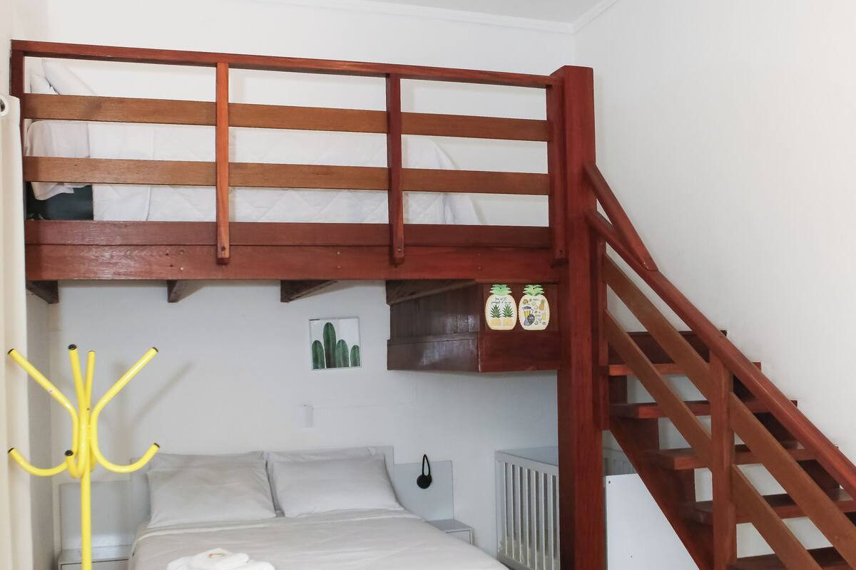 Quarto com beliche, escada de madeira, radiador e cabideiro amarelo.