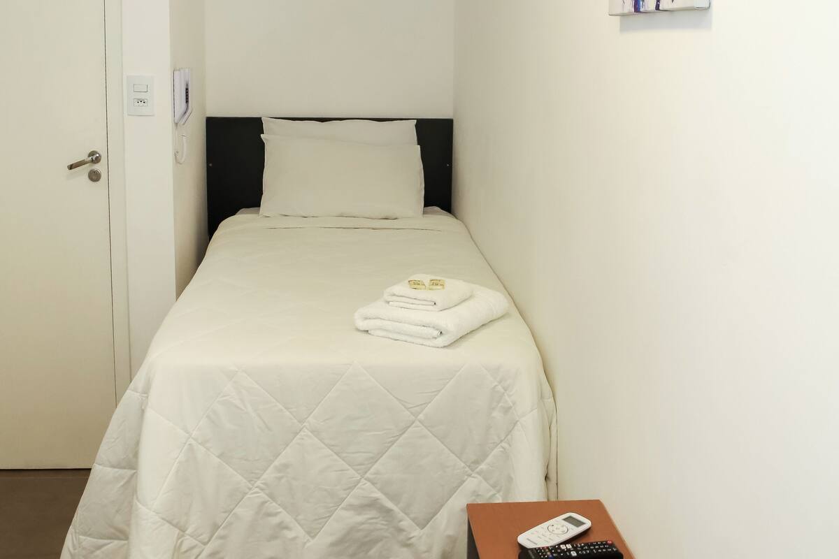 Quarto com cama, mesa de cabeceira com controle remoto e duas pinturas na parede.