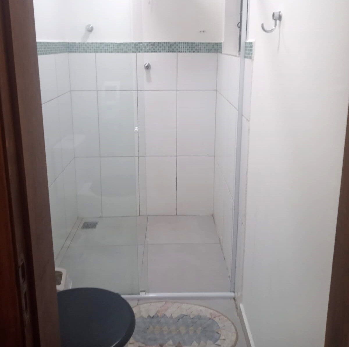 Um chuveiro pequeno e fechado, com azulejos brancos e uma borda verde.