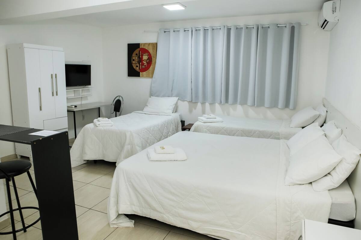 Quarto de hotel com duas camas, uma escrivaninha, uma cadeira, uma televisão e uma cortina.