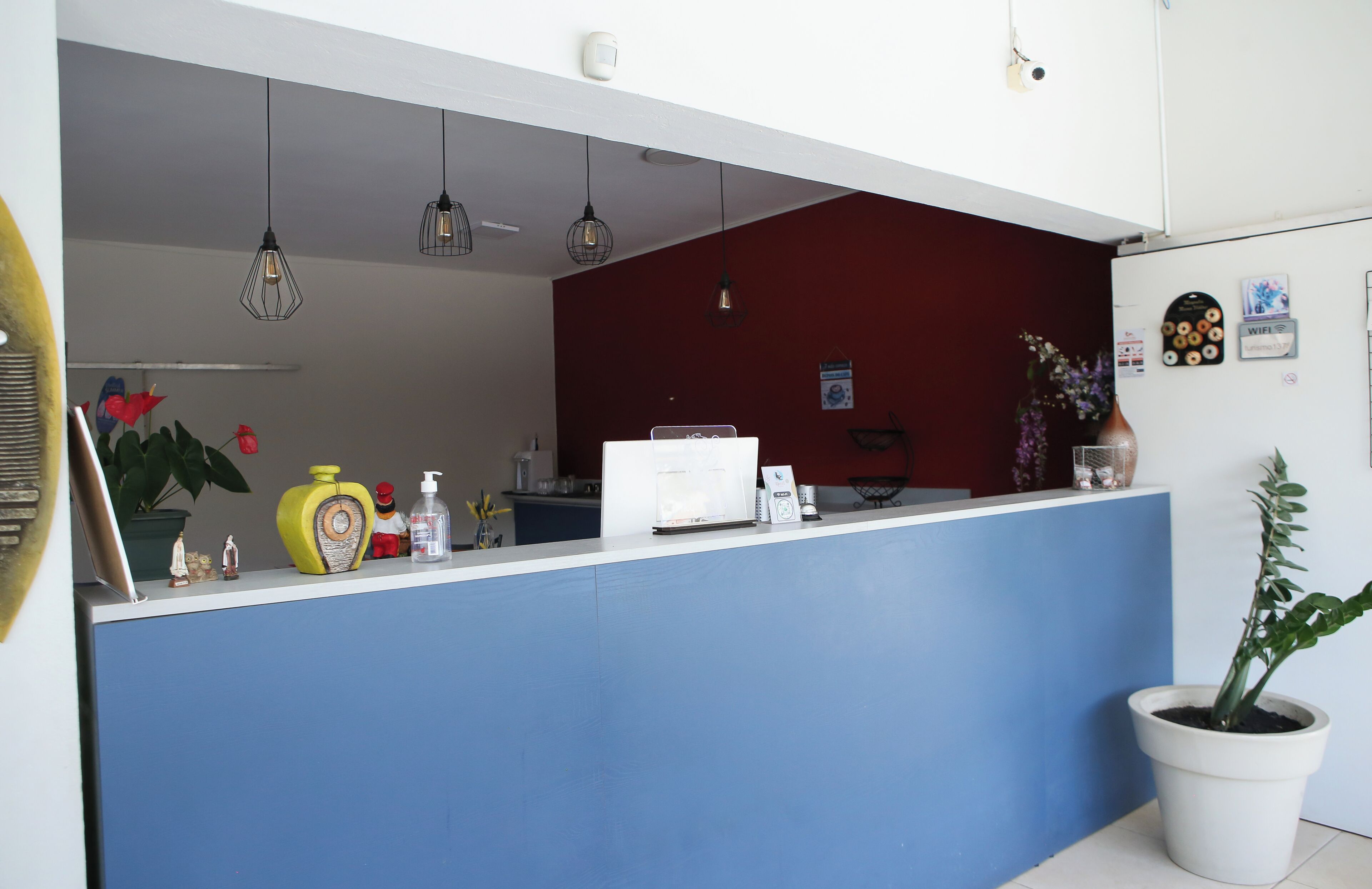 A reception area with a blue counter, a red wall, hanging pendant lights, a potted plant, and a refrigerator with a WiFi sign.