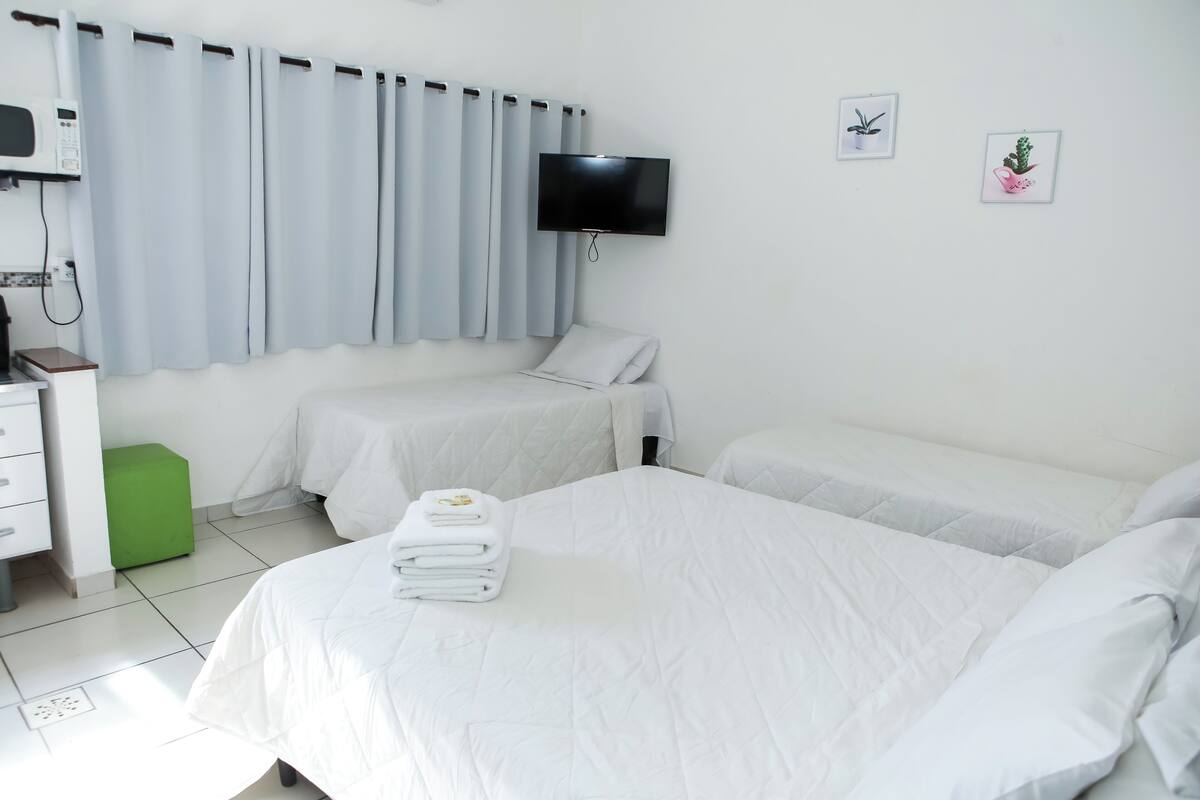 Quarto de hotel com duas camas, uma televisão de tela plana, um micro-ondas e um banquinho verde pequeno.