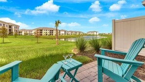 A patio area with a table and chairs, a small pond, and a view of apartment buildings. - Margaritaville 3 bedroom home 3201 (Kissimmee)