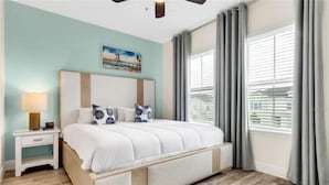 A bedroom with a bed, nightstand, lamp, and a painting on the wall. - Margaritaville 3 bedroom home 3201 (Kissimmee)