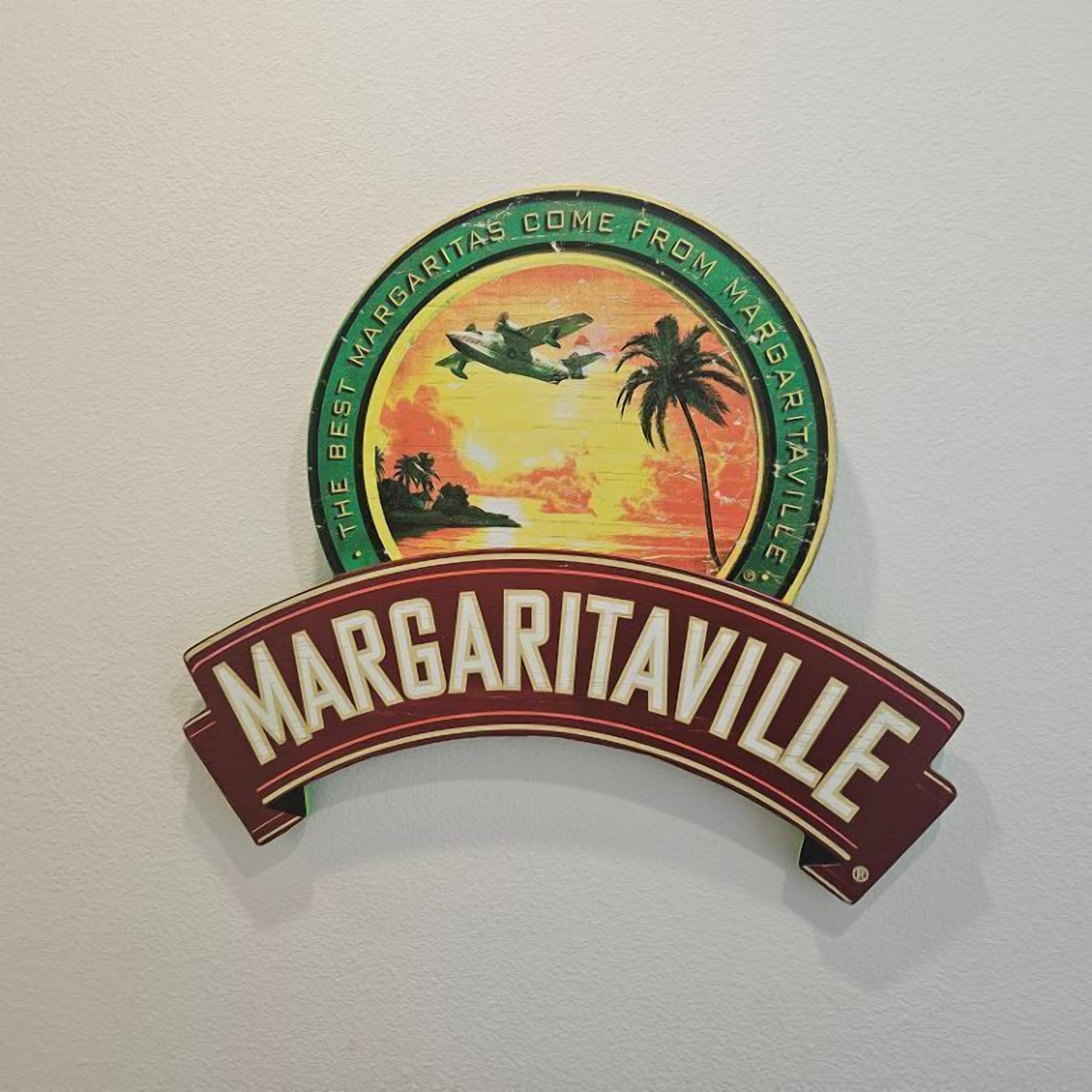 A wall-mounted sign with a sunset scene, palm trees, and an airplane, featuring the text "Margaritaville".
