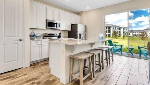 A modern kitchen with white cabinets, a central island with stools, a microwave, and a refrigerator. - Margaritaville 3 bedroom home 3201 (Kissimmee)