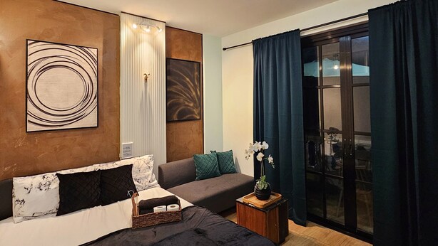 A modern bedroom with a large bed, a sofa, and a small table. There is a window with curtains, a ceiling light, and artwork on the wall. - Cinema Stay inside Intramuros Manila by IN CAFE (Manila)