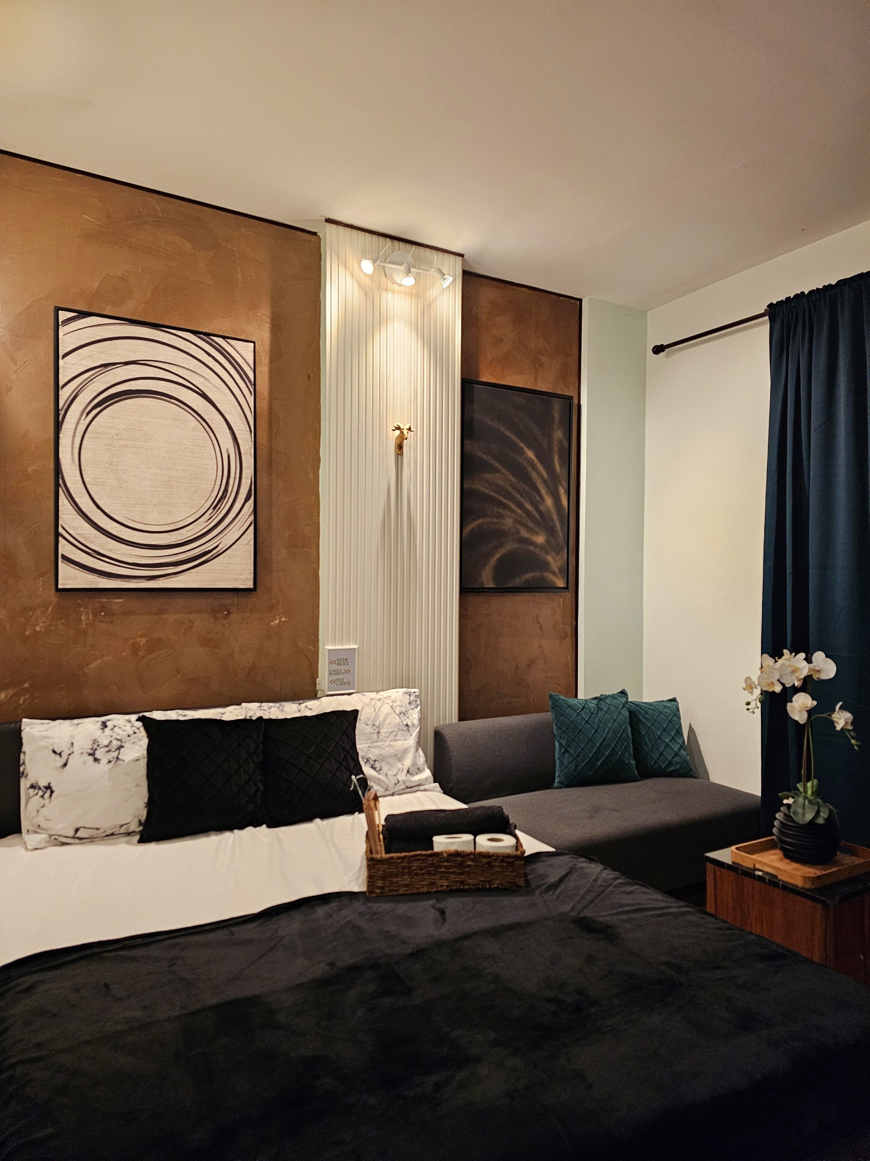 A modern bedroom with a large bed, a smaller sofa, and a decorative wall with abstract art.