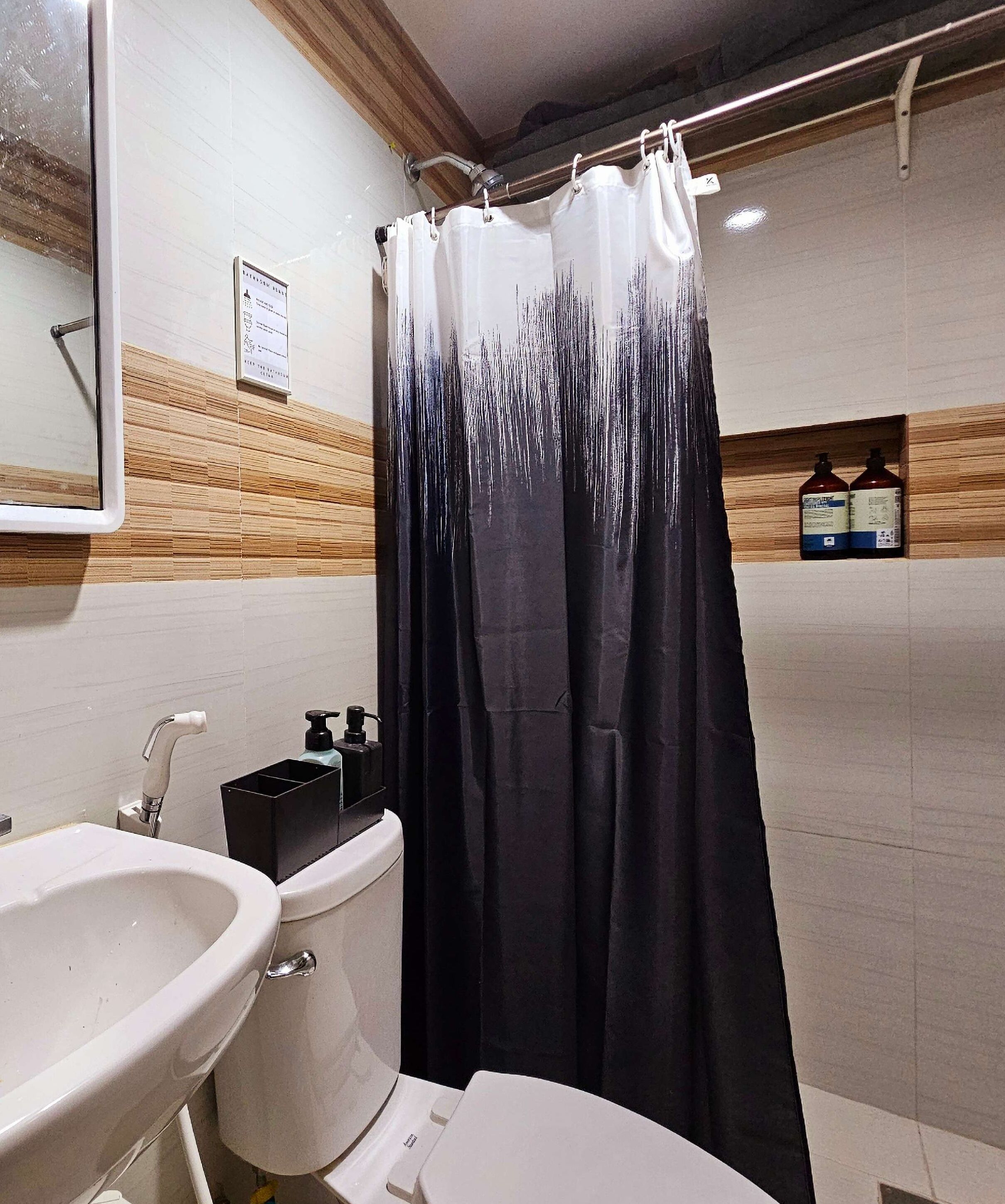 A bathroom with a white sink, a toilet, a shower curtain with a tree design, and two bottles of shampoo on a shelf.