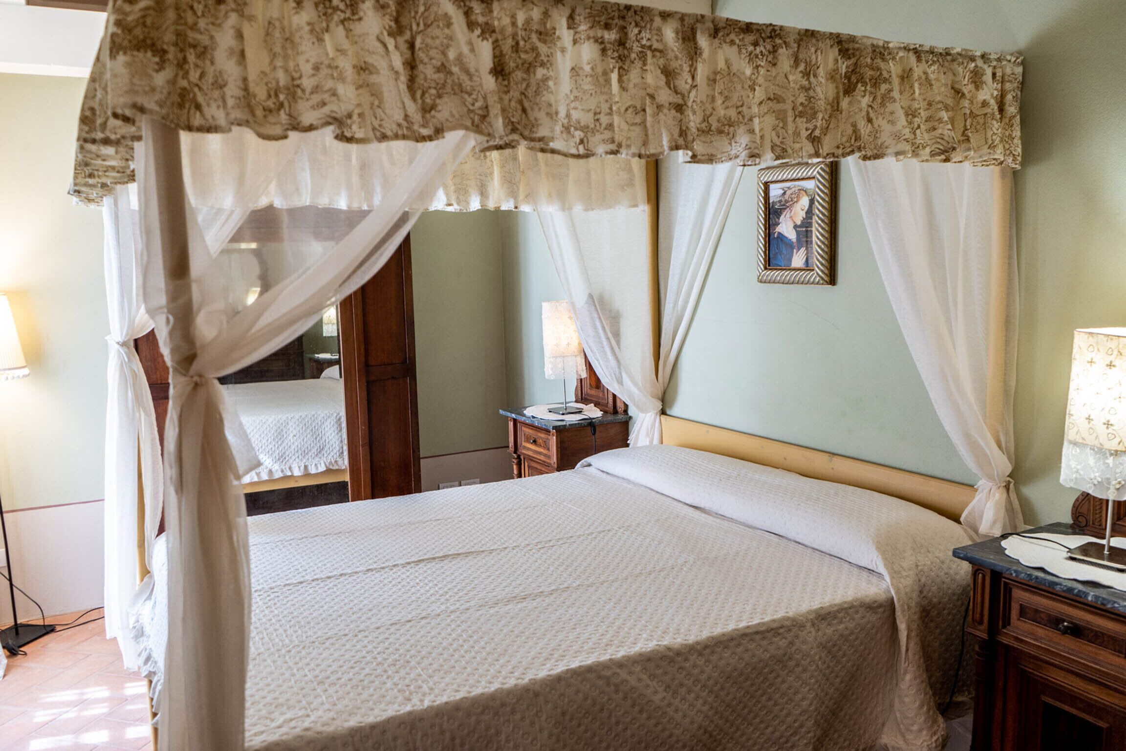 A bedroom with a canopy bed, a bedside table with a lamp, and a nightstand.