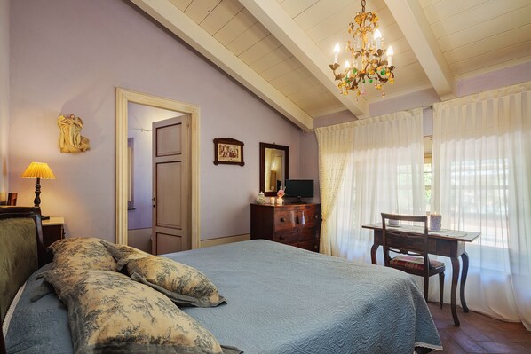 A bedroom with a bed, a desk, a chair, a lamp, a mirror, and a chandelier.