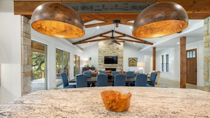 A spacious dining area with a large granite table, blue chairs, and a stone fireplace. - ⭐️⭐️LUXURY WATERFRONT-CHEF’S KITCHEN-FIRE PIT-SLEEPS 24⭐️⭐️ (Horseshoe Bay)