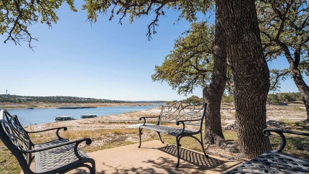 Un banc et un arbre au bord d’une étendue d’eau calme, sous un ciel dégagé.