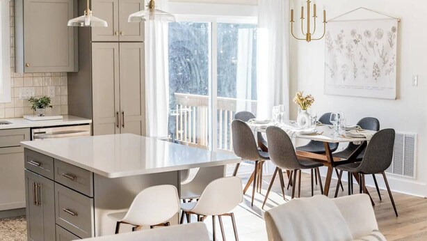A modern kitchen with a large island, dining area with chairs, pendant lights, and a large window with a view. - Sleeps 20 | Family-friendly | Near DT LYH & LU (Madison Heights)