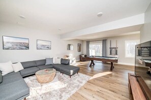 A modern living room with a sectional sofa, a pool table, and a large window. - Sleeps 20 | Family-friendly | Near DT LYH & LU (Madison Heights)