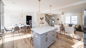 A spacious kitchen with a central island, a dining area with chairs and a table, a living room with a sofa and a coffee table, and a staircase leading to another level. - Sleeps 20 | Family-friendly | Near DT LYH & LU (Madison Heights)