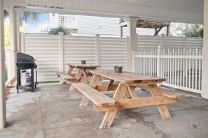 A covered outdoor area with a picnic table, a grill, and a white fence. - Reel Time  6 BD St George Island, FL Vacation Re (St. George Island)