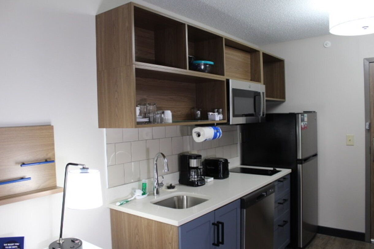 A compact kitchen with a microwave, refrigerator, and sink. There are wooden cabinets above the counter and a blue cabinet below.