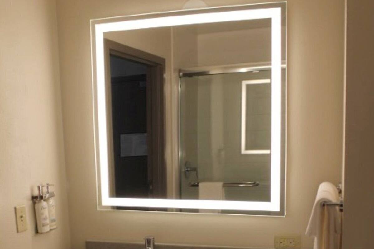 A bathroom with a large mirror, two sinks, a towel rack, and a toilet.
