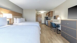 A hotel room with two beds, a desk, a chair, a microwave, and a TV.