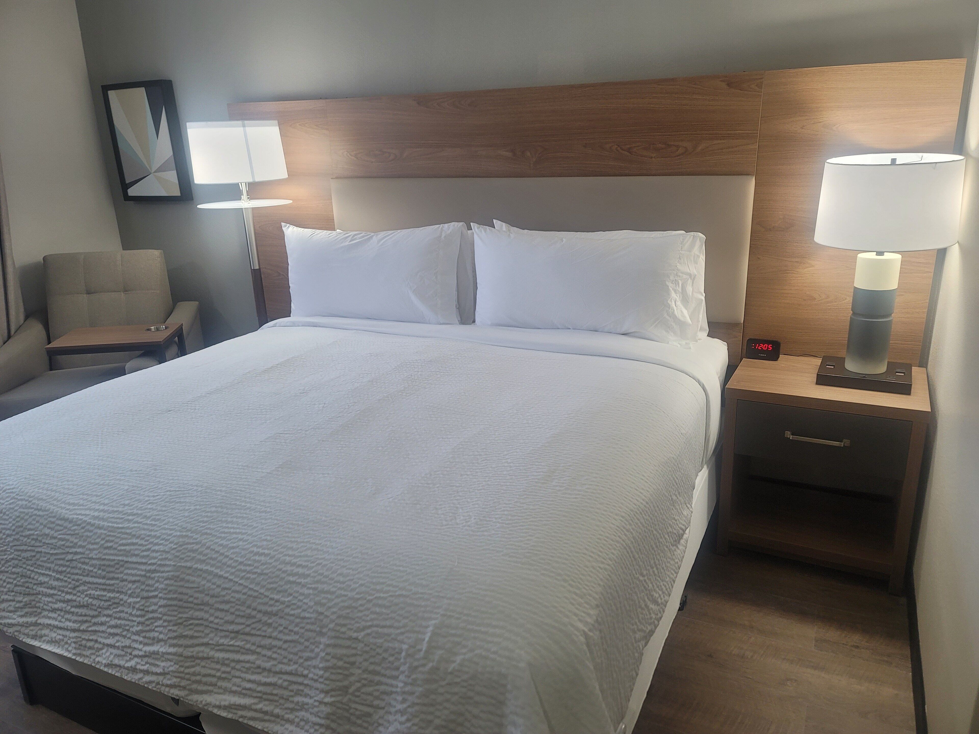 A hotel room with a large bed, two bedside tables, a chair, and a nightstand with a lamp.