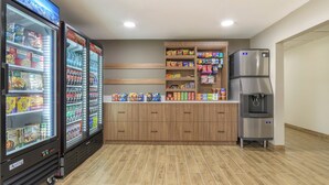 A kitchenette with a refrigerator, a coffee machine, and shelves stocked with snacks and beverages.
