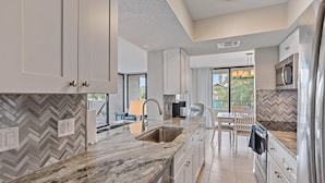 A modern kitchen with marble countertops, stainless steel appliances, and a herringbone tile backsplash. - Across Street to Main Beach Access, Tennis, Heated Pool (Siesta Key)
