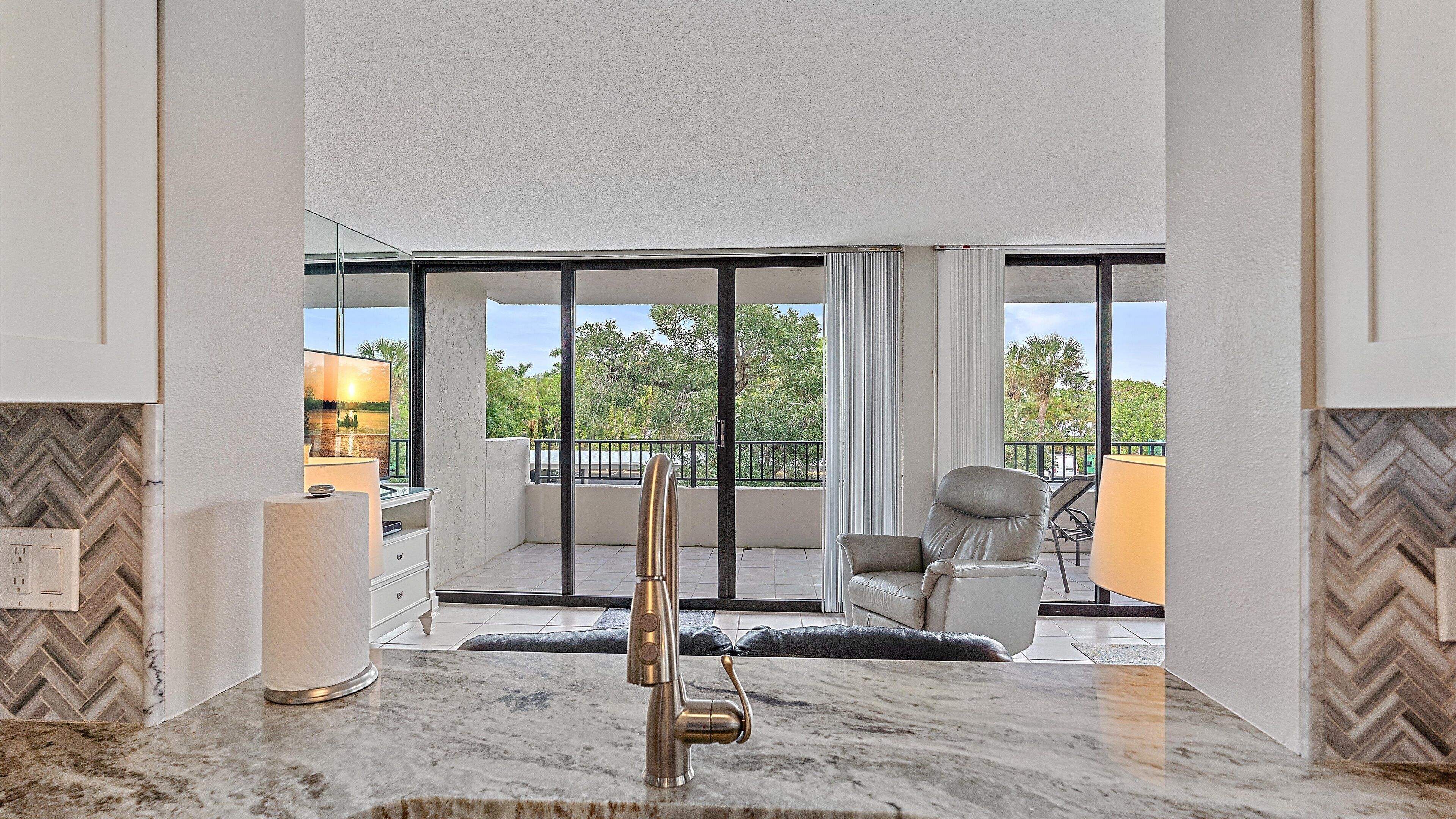 A modern kitchen with a large window, a marble countertop, and a view of the outdoors.