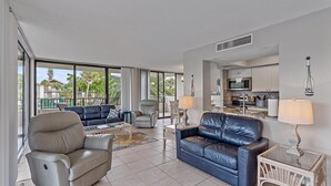 A spacious living area with a sofa, armchairs, a coffee table, and a dining table. A kitchen is visible in the background. - Across Street to Main Beach Access, Tennis, Heated Pool (Siesta Key)