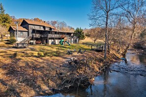 A rustic cabin with a wooden deck and a green slide, situated by a calm river. - River Access! Kayak/ Fire pit/ Hot Tub/ Top 10% (Sevierville)