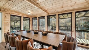 A wooden-paneled room with a large table and chairs, large windows with blinds, and a view of trees outside. - River Access! Kayak/ Fire pit/ Hot Tub/ Top 10% (Sevierville)