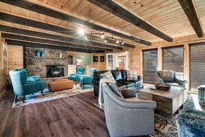 A spacious living room with a stone fireplace, wooden beams, and modern furniture.