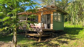 A small wooden cabin with a porch, surrounded by trees and greenery. - Kukui Cabin with Private Bath (Kealakekua)