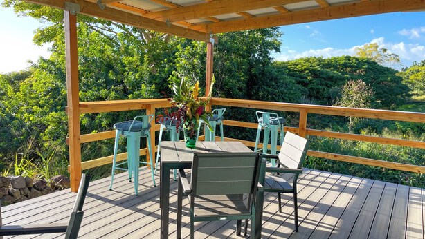 A wooden deck with a pergola, outdoor seating, and a view of lush greenery. - Kukui Cabin with Private Bath (Kealakekua)