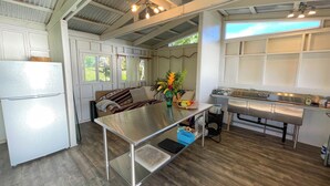 A compact kitchen with a central island, a refrigerator, and a dining table. - Kukui Cabin with Private Bath (Kealakekua)