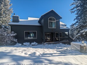 A two-story house with a dark exterior, a large front porch, and a chimney.