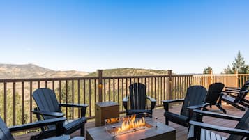 A deck with Adirondack chairs, a fire pit, and a view of mountains.