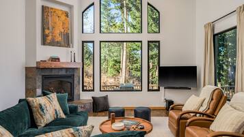 A modern living room with a fireplace, large windows, a sofa, a leather chair, and a flat-screen TV.