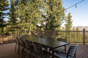 A wooden deck with a table and chairs, surrounded by trees and a mountain view.